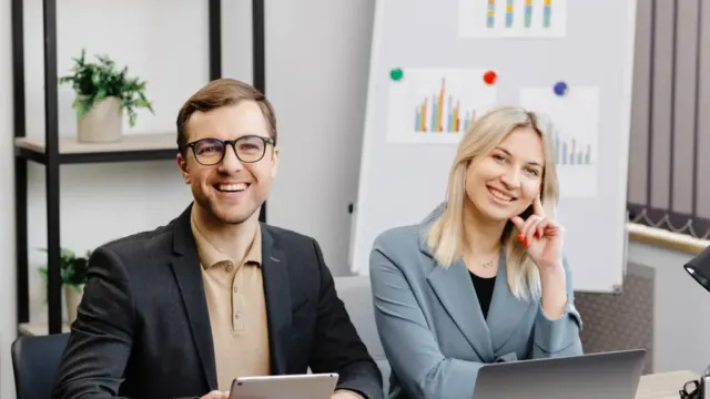 Two colleagues smiling in a meeting room with charts behind them