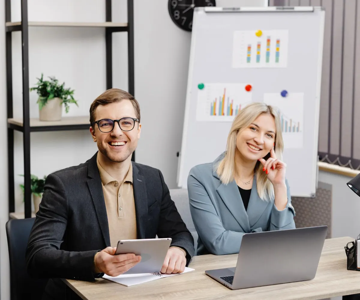 Two colleagues smiling in a meeting room with charts behind them