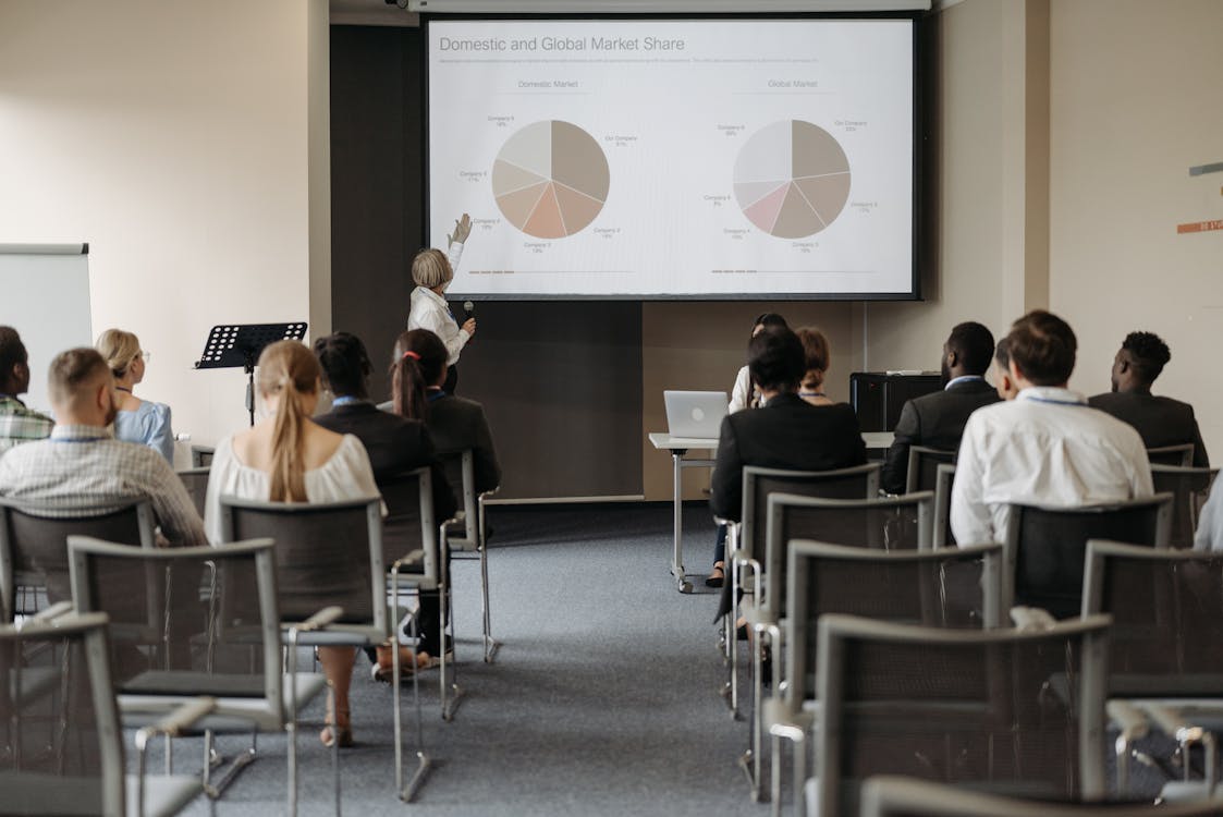Diverse audience seated in rows attentively watching a speaker present data at a business conference.